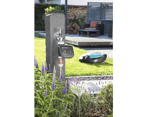 Scéna s vodovodním kohoutkem, zavlažovacím počítačem Gardena, zavlažovačem trávníku a robotickou sekačkou na zahradě.