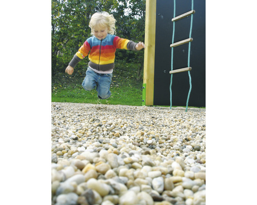 Dítě skáče na hřišti vedle lezecké stěny a provazového žebříku.