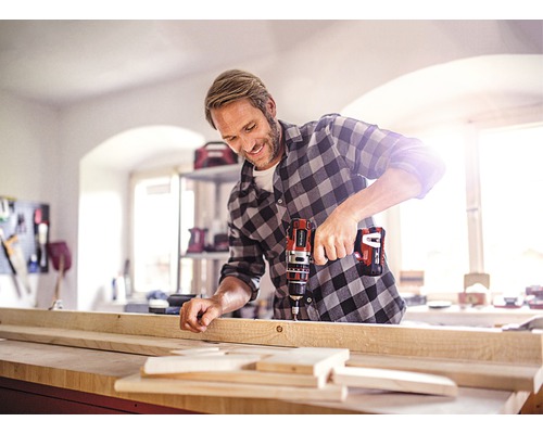 Řemeslník vrtá aku šroubovákem dřevěnou desku na ponku