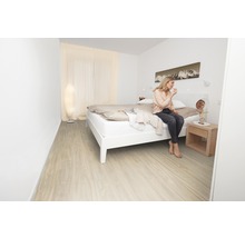 Světlá ložnice s postelí, nočním stolkem a ženou, která se líčí