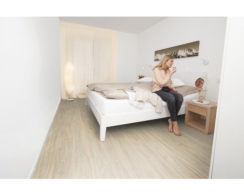 Světlá ložnice s postelí, nočním stolkem a ženou, která se líčí