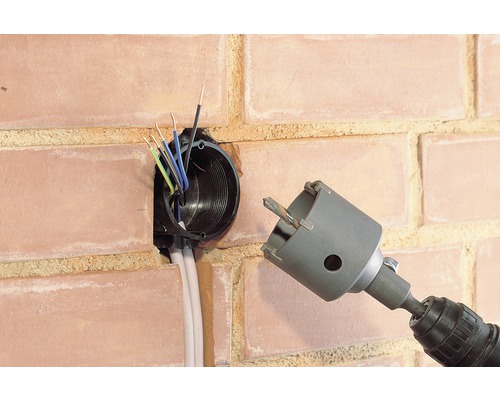 Vrtací stroj s děrovkou vedle nástěnné zásuvky v cihlové zdi