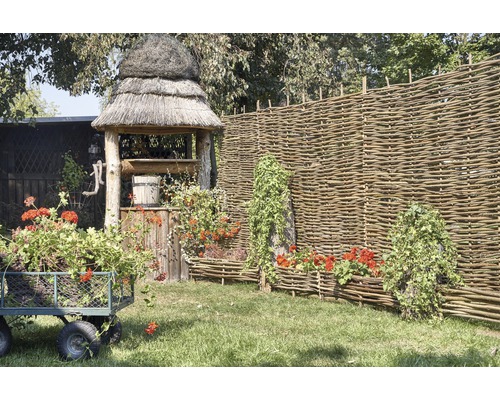 Scéna s zahradní studnou, proutěným plotem, květinovým vozíkem a osázenými proutěnými truhlíky