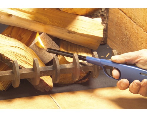 Osoba zapaluje palivové dřevo tyčovým zapalovačem