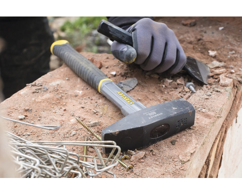 Kladivo, sekáč a pracovní rukavice leží na zdi.