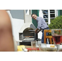 Muž griluje maso grilovacími kleštěmi na zahradním grilu.