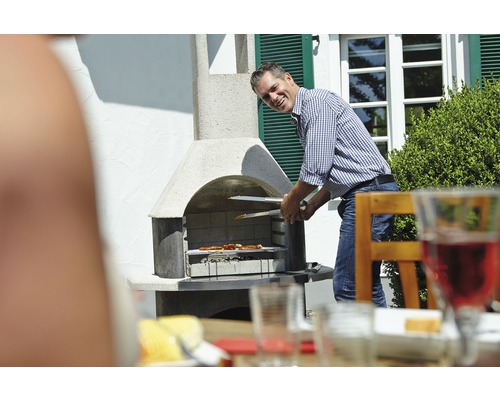 Muž griluje maso grilovacími kleštěmi na zahradním grilu.