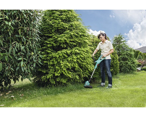 Žena používá strunovou sekačku na zahradě.