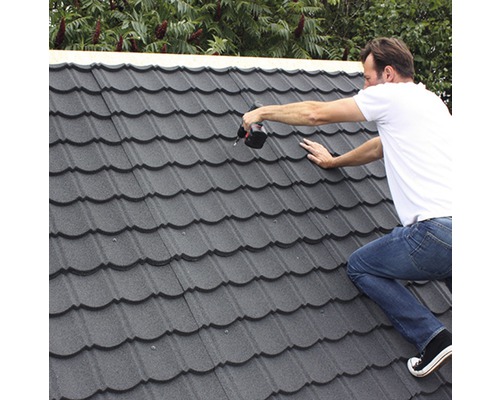 Řemeslník montuje kovové střešní tašky pomocí akumulátorového šroubováku