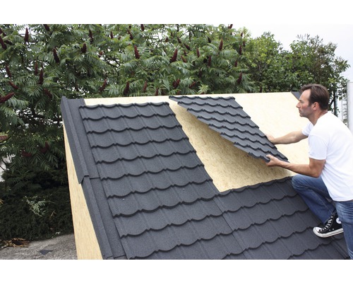 Muž pokládá kovové střešní tašky na střechu.