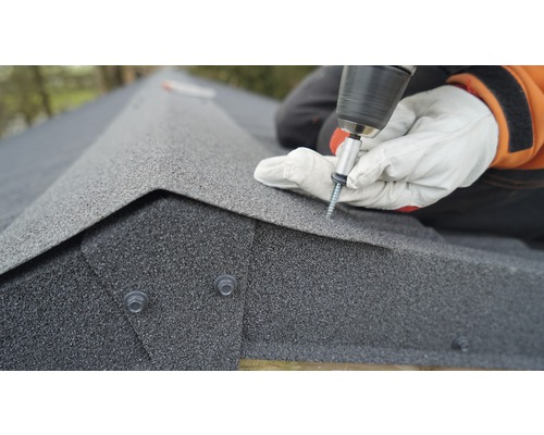 Osoba připevňuje střešní šindele šroubovákem.