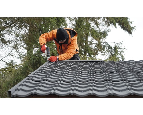Řemeslník montuje střešní tašky pomocí akumulátorového šroubováku