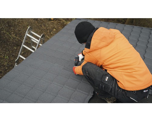 Řemeslník připevňuje střešní tašky aku šroubovákem na střechu