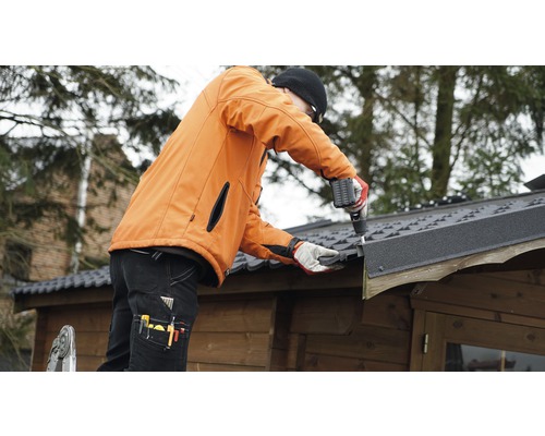 Řemeslník montuje střešní lepenku na zahradní domek pomocí akumulátorového šroubováku.