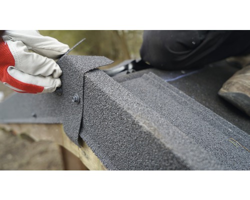 Detailní záběr instalace střešních šindelů pomocí šroubů osobou v rukavicích.