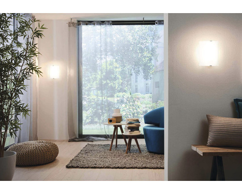 Obývací pokoj s nástěnnými svítidly, okny se závěsy, odkládacími stolky a dekorativními prvky.