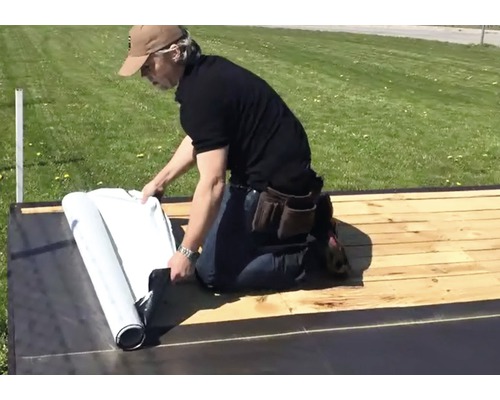 Osoba rozvíjí střešní krytinu na dřevěné střeše.