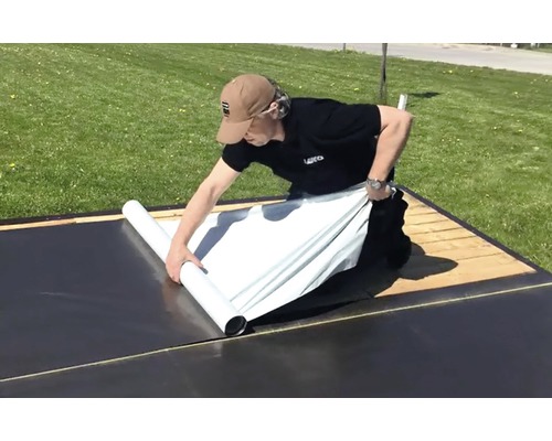 Osoba rozkládá střešní krytinu na střeše.