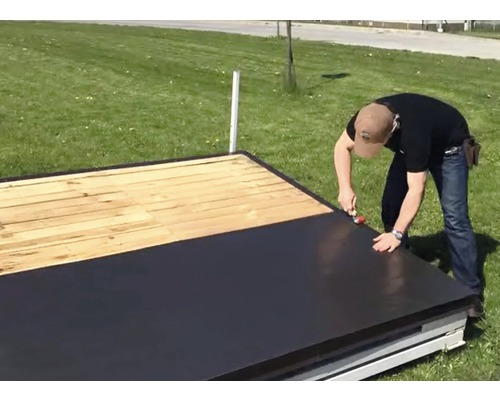 Muž pokládá střešní lepenku na dřevěnou střechu