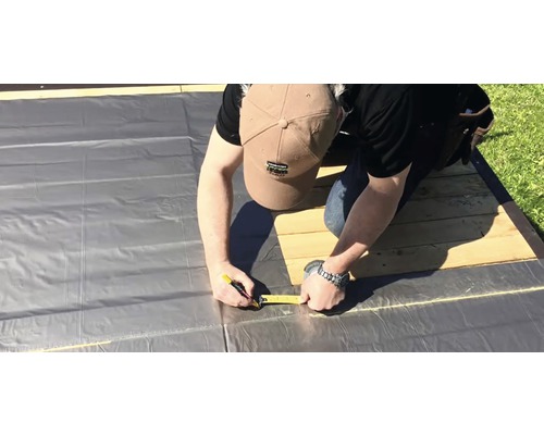 Muž měří fólii svinovacím metrem pro stavební práce.