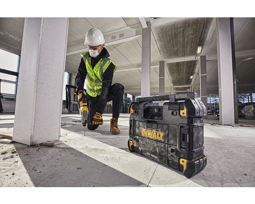 Stavební dělník vrtá vrtačkou v budově, vedle něj nabíječka Dewalt.