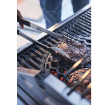 Maso se obrací grilovacími kleštěmi na grilu.