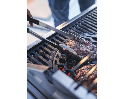 Maso se obrací grilovacími kleštěmi na grilu.
