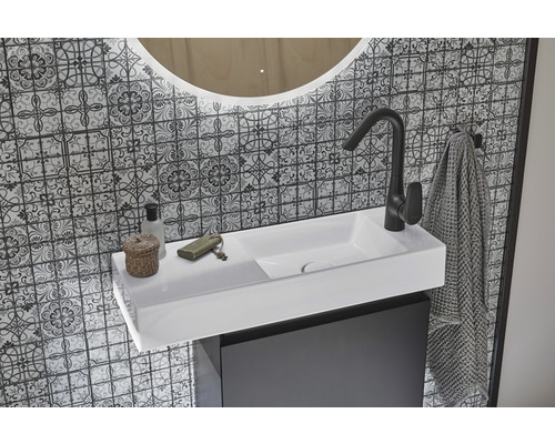 Koupelnové umyvadlo s baterií, ručníkem a zrcadlem před vzorovanou stěnou