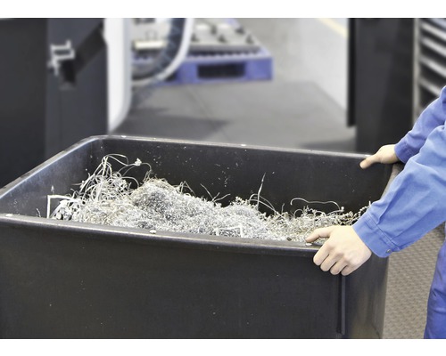 Osoba drží černou vanu naplněnou kovovými třískami.