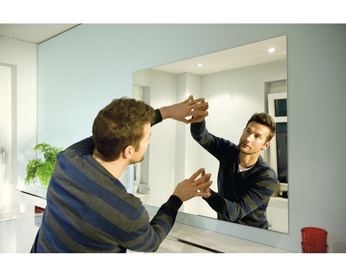 Muž připevňuje obdélníkové zrcadlo na zeď