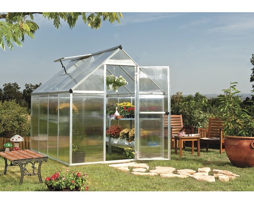 Skleník s otevřenými dveřmi a policemi plnými květin v zahradě.