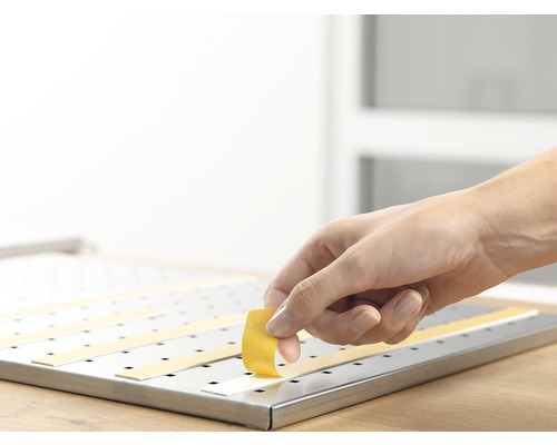 Osoba připevňuje lepicí pásky na děrovaný panel.