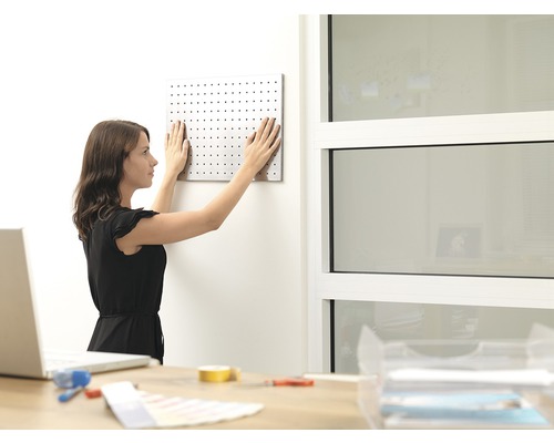 Žena připevňuje děrovanou desku na zeď v pracovně