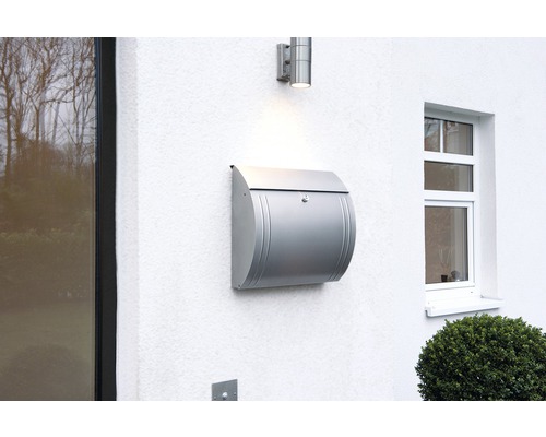 Stříbrná poštovní schránka na bílé zdi vedle lampy a okna