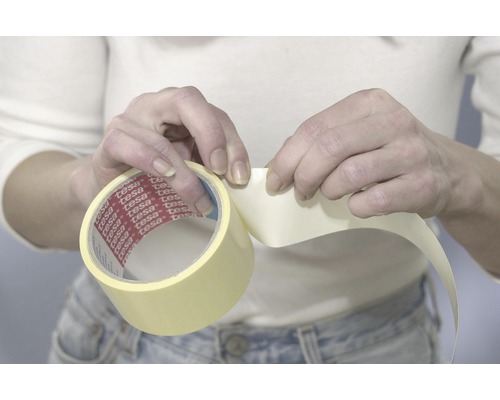 Osoba drží v rukou roli maskovací pásky Tesa.