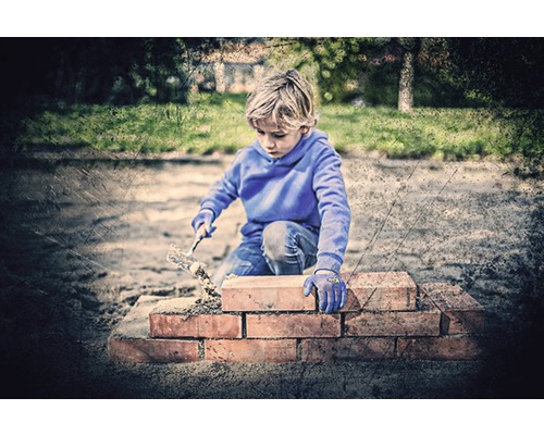 Chlapec staví zeď z cihel a lžíce