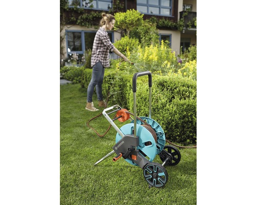 Žena používá zahradní hadicový vozík Gardena na zahradě