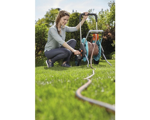 Žena obsluhuje vozík na hadici na zahradě se zahradní hadicí