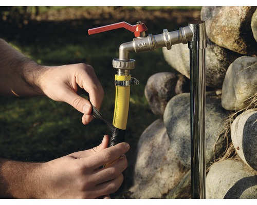 Osoba připevňuje kus žluté zahradní hadice k vodovodnímu kohoutku pomocí černé izolační pásky.