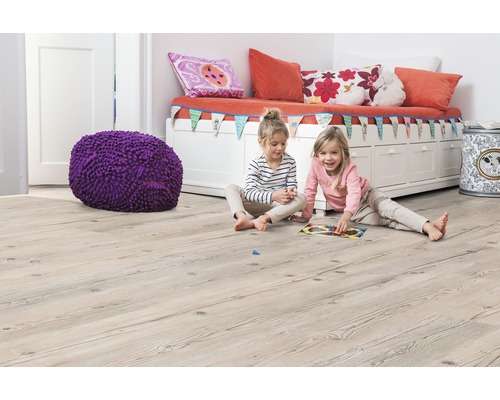 Dětský pokoj se světle hnědou dřevěnou podlahou, lavicí, polštáři, hračkami a dvěma hrajícími si dívkami