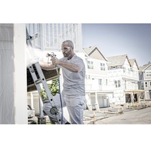 Muž na žebříku natírá dům stříkací pistolí