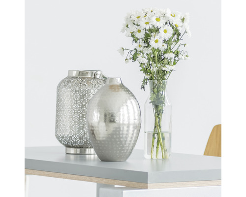 Dekorativní scéna s lucernou, vázou a kyticí na stole.