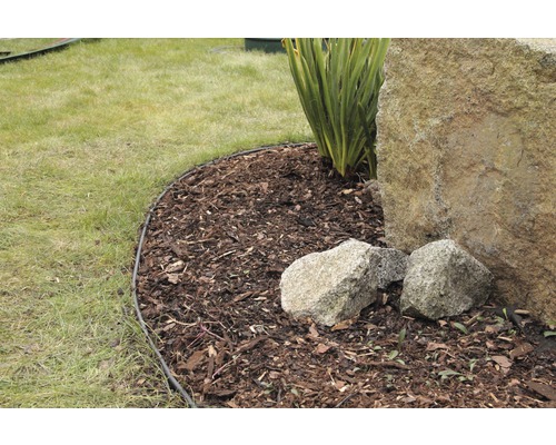 Zahradní scéna s okrajem trávníku, mulčovací kůrou, kamenem a rostlinou