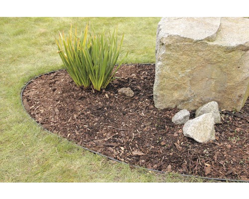 Zahrada s trávníkem, rostlinami a velkým kamenem, ohraničená obrubníkem trávníku