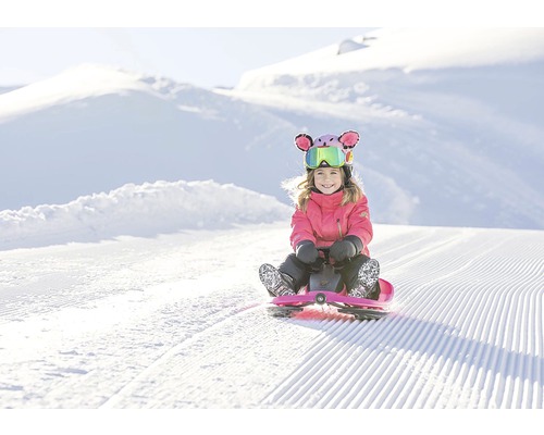 Dítě jezdí na sáňkách po zasněženém svahu.