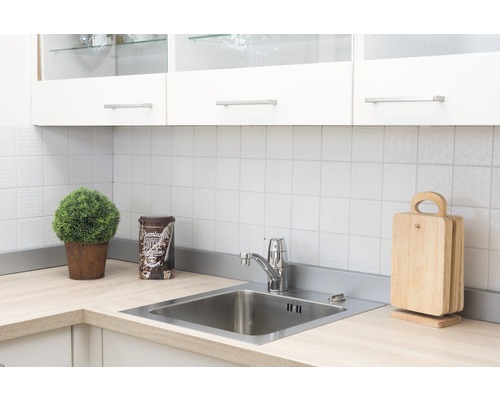 Kuchyňská scéna s dřezem, baterií, krájecími deskami a dekorací na světlé pracovní desce před bílým obkladem