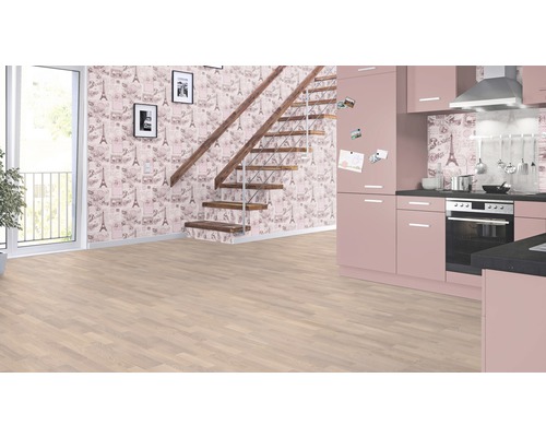 Světlá místnost s laminátovou podlahou, schodištěm, vzorovanou tapetou a růžovou kuchyní