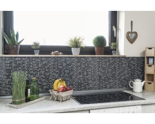 Kuchyňská scéna s mozaikovými dlaždicemi, parapet s rostlinami, košík s ovocem a varná deska.