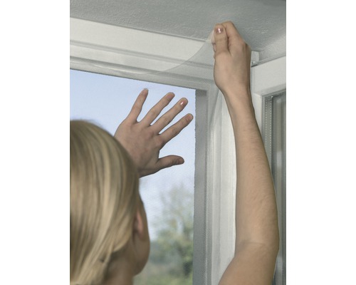 Osoba upevňuje síť proti hmyzu na okno