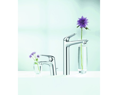 Dvě umyvadlové baterie z kovu různých velikostí s květinami ve sklenicích.